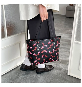 Close-up of a large black tote bag with cherry prints held by a model in casual attire