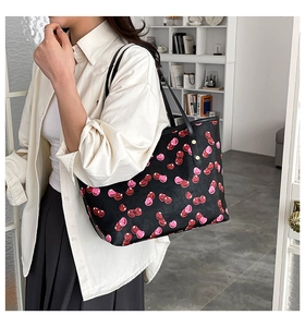 Detail of a black tote bag with heart cherry print and gold rivets on a model