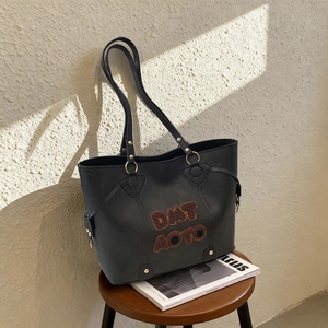 Chic black leather tote bag with plush brown letter embroidery on a high-end wooden stool