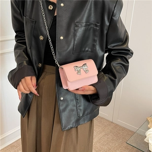 Détail d'un mini sac rose avec un grand nœud métallique argenté et une bandoulière chaîne