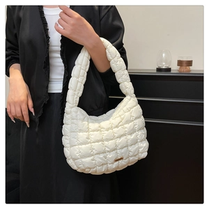 Detail view of white quilted puffer bag with golden metal hardware on black dress backdrop