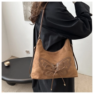 Brown suede shoulder bag with butterfly patch and leather lace-up detail on model