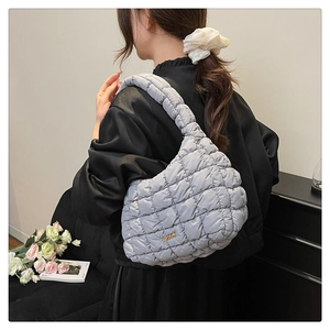 Detail of grey quilted shoulder bag with puffy fabric and golden metal logo plaque