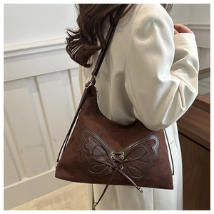 Close-up of brown suede shoulder bag featuring a large leather butterfly applique and bow
