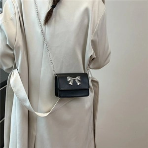 Vue arrière d'un mini sac à rabat noir avec noeud argenté et bandoulière chaîne sur modèle