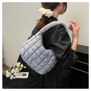 Detail of light grey quilted puffy shoulder bag with golden metal hardware on model