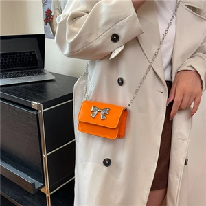 Détail d'un mini sac bandoulière orange brillant avec un nœud argenté et une chaîne