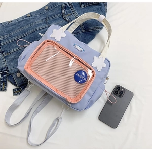 Dettaglio borsa di tela lavanda con tasca in rete rosa ed emblema blu FASHION su sfondo bianco