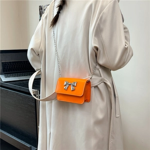 Détail du sac bandoulière orange vif avec un nœud argenté et une bandoulière chaîne