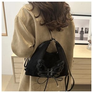 Detail of black suede shoulder bag featuring a leather butterfly motif and ribbon ties