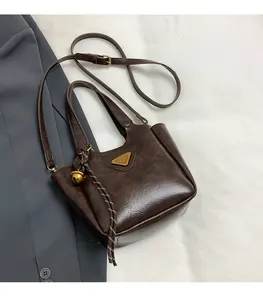 Detail view of coffee brown tote bag with metallic triangle logo and gold bell charm