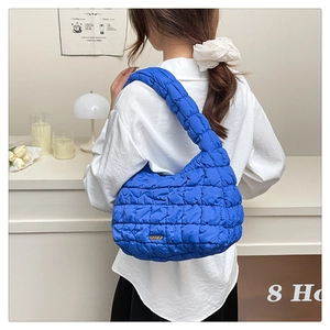 Detail of blue quilted baguette bag with ruffled texture and golden logo plate