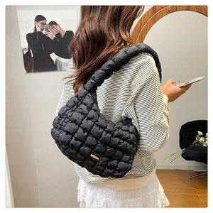 Detail view of black quilted puff shoulder bag worn underarm with gold plaque logo