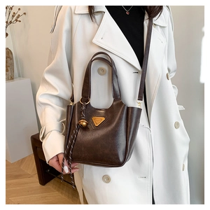 Detail view of the deep brown leather tote with a gold triangular logo and bell charm