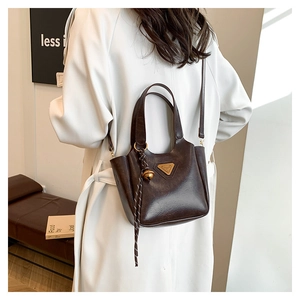 Detail of dark brown tote bag on model in white trench coat with pendant accessory