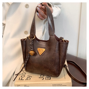 Close-up of retro brown tote bag featuring metallic logo and vintage bell charm detail