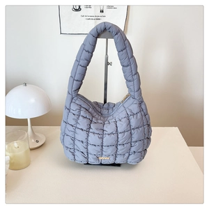 Detailed macro view of quilted blue shoulder bag with golden logo plaque and zipper texture