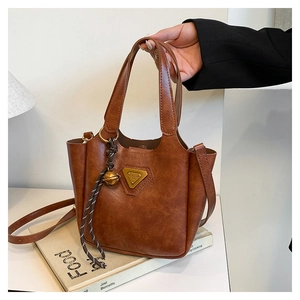 Close-up of brown vintage leather tote bag with gold triangle plaque and bell charm detail