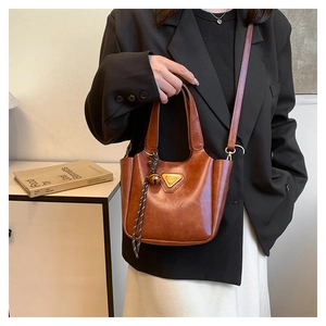 Detail of retro brown leather tote with gold logo and bell charm on a model