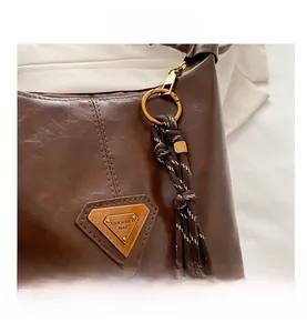Detail of dark brown retro shoulder bag with metallic logo and bell charm pendant