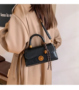 Detail view of black leather handbag with gold twist lock and woven strap on model