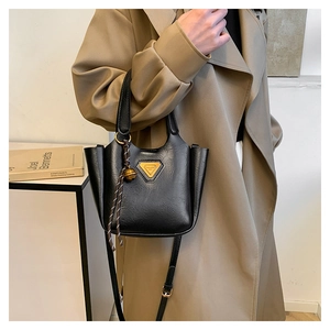 Detail of black lychee grain leather tote bag with metal logo and woven knot charm
