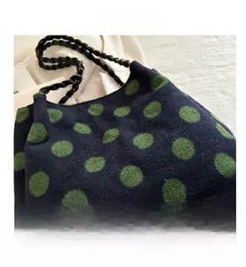 Detail of navy knit tote bag featuring green polka dots and a black braided handle