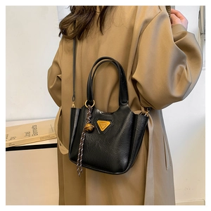 Detail of black glossy PU leather tote bag with gold hardware and woven pendant