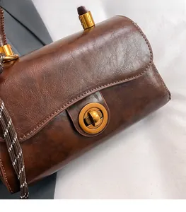 Close-up of vintage brown leather bag featuring a gold round lock and woven shoulder strap