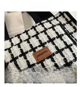 Detail shot of black and white tweed tote bag with a brown leather logo patch decoration