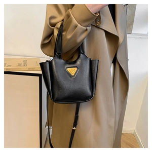 Detail of a vintage black leather bucket bag with a golden triangle logo on a trench coat