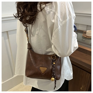 Close-up of vintage brown oil-wax leather shoulder bag with triangle logo and bell charm