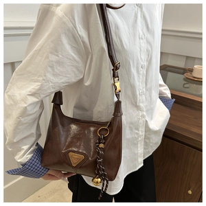 Detail of vintage brown leather hobo bag with metal logo and woven bell pendant