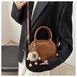 Detail of a brown leather crossbody bag featuring a golden buckle and a cute bear charm