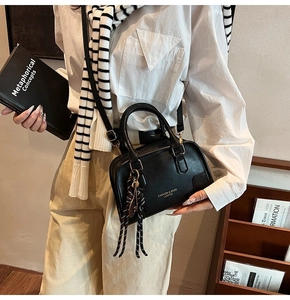 Close-up of black leather boston bag with woven tassel and adjustable strap on a model