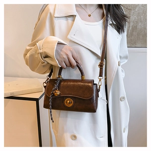 Close-up of retro brown leather handbag with metal lock and decorative striped rope charm