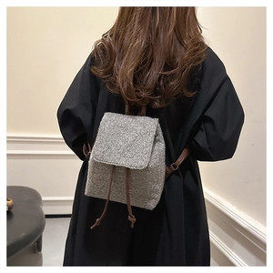 Rear view of a model wearing a minimalist grey felt backpack with brown leather drawstrings