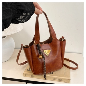 Detail of vintage brown tote bag with metal triangle plaque and decorative bell charm