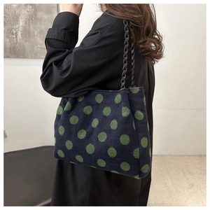 Detailed texture of the plush tote bag featuring green polka dots and woven black chain
