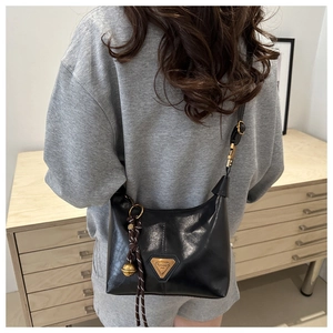 Detail of black leather shoulder bag with gold triangular plaque and woven pendant