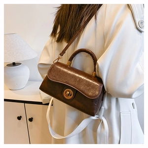 Brown vintage leather handbag with gold clasp shown on model in a modern interior setting