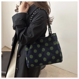 Detail of navy plush tote bag with green polka dots and black braided leather handle