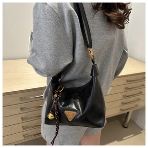 Detail shot of black leather shoulder bag featuring a triangle logo and woven charm