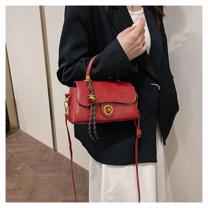 Detail of red vintage crossbody bag with gold twist lock and woven bell pendant charm