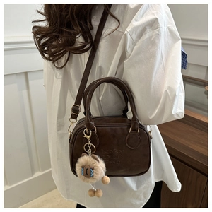 Detail of a dark brown mini square bag with Lucky engraving and a plush lion charm