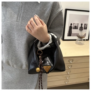 Detail of black leather handbag with a triangle logo and golden bell tassel charm