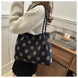 Detail view of navy plush tote bag with gold dots and black woven rope handle worn by model