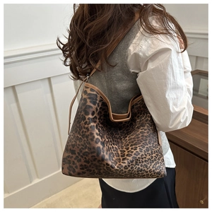 Detailed view of large leopard print hobo tote bag with brown leather trim on woman's shoulder