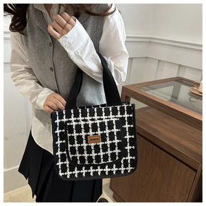 Detail of black and white tweed check tote bag with brown leather logo and black handles