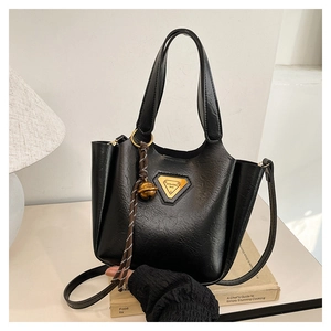 Detail of black leather tote bag featuring golden triangle logo and small bell charm